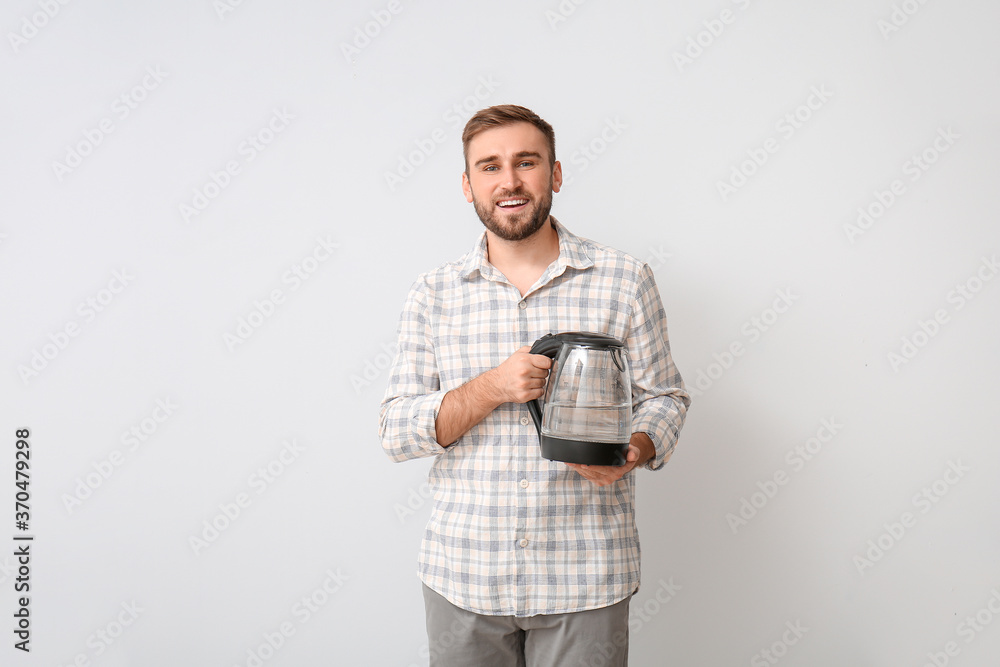 Young man with electric kettle on light background