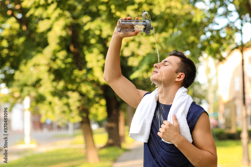 Sporty young man pouring water on himself in park