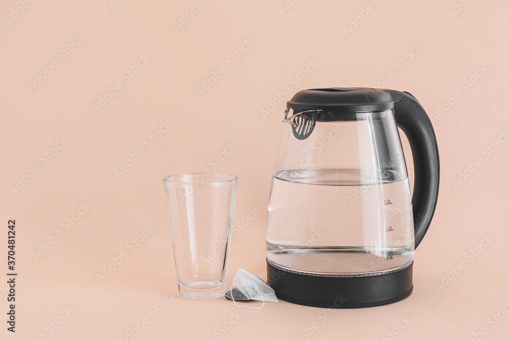 Electric kettle with glass and tea bag on color background