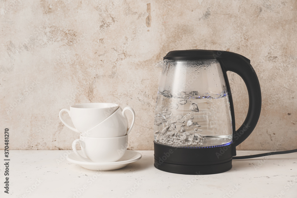 Modern electric kettle and cups on table