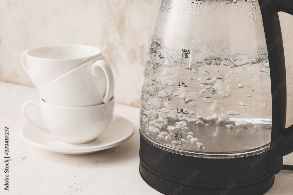 Modern electric kettle and cups on table