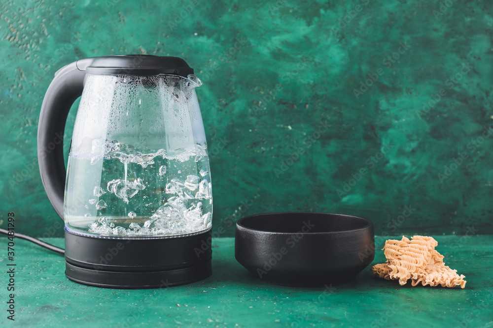 Modern electric kettle, bowl and raw pasta on table