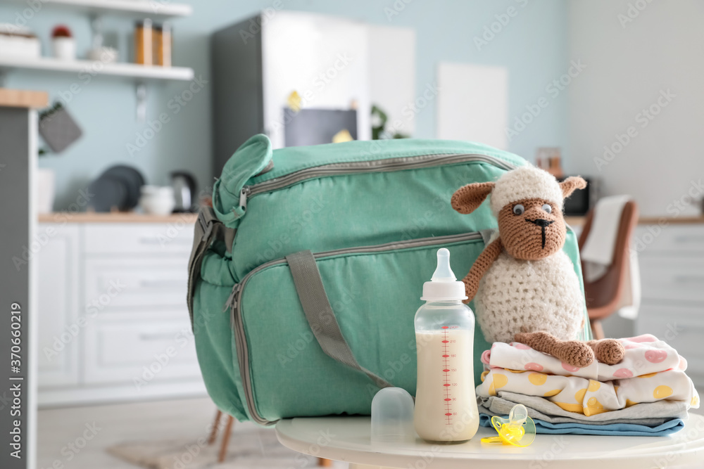 Bottle of milk for baby, bag, clothes and toy on table