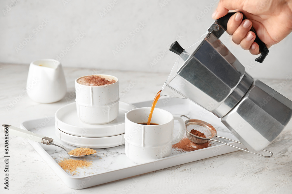 Woman pouring hot coffee from pot into cup on table