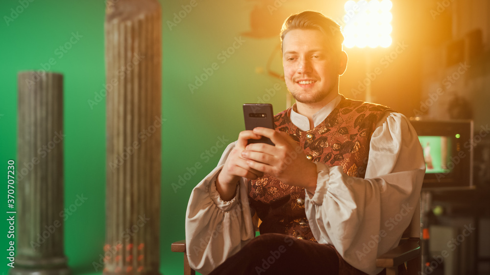 On Period Drama Film Set: Handsome Actor Wearing Historical Costume Sitting in a Chair on a Break Us