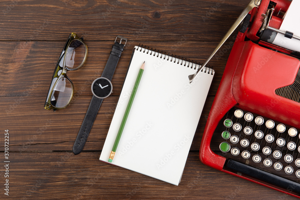 Writer or journalist workplace - vintage red typewriter, glasess and notepad on the wooden desk