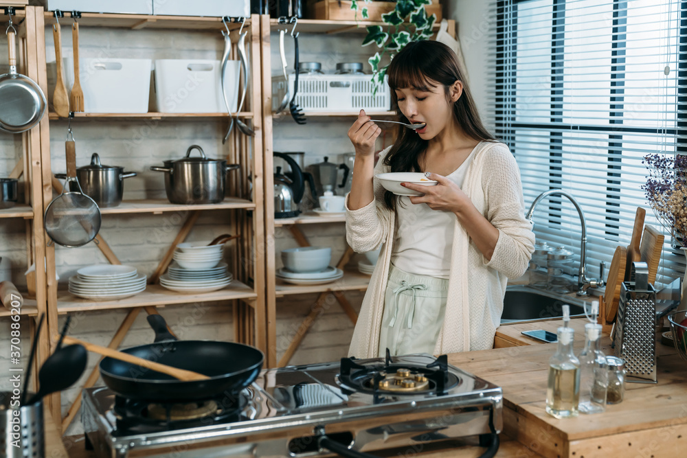 年轻女士用酸奶做了一种新口味的麦片，在厨房里品尝健康的早餐