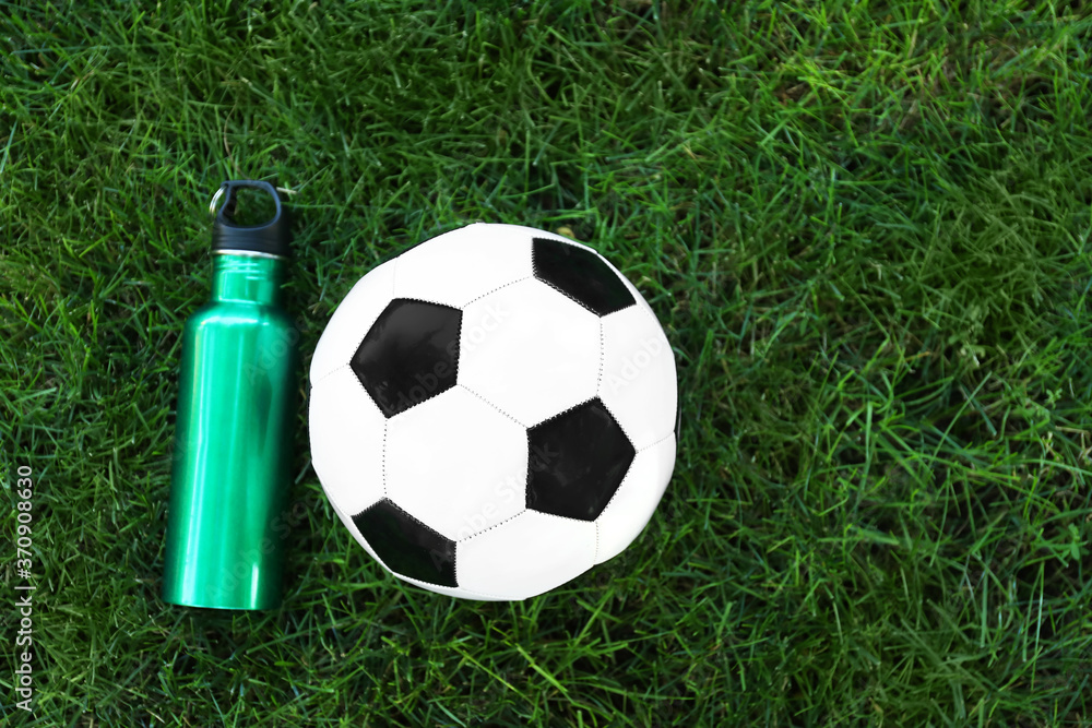 Soccer ball and bottle of water on green grass outdoors