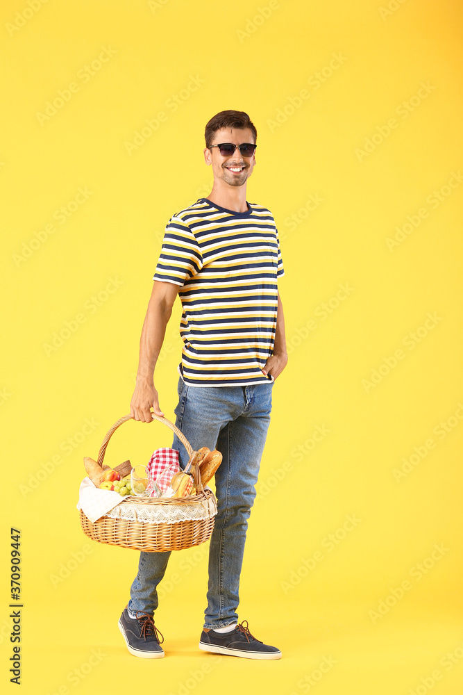 Young man with food for picnic in basket on color background