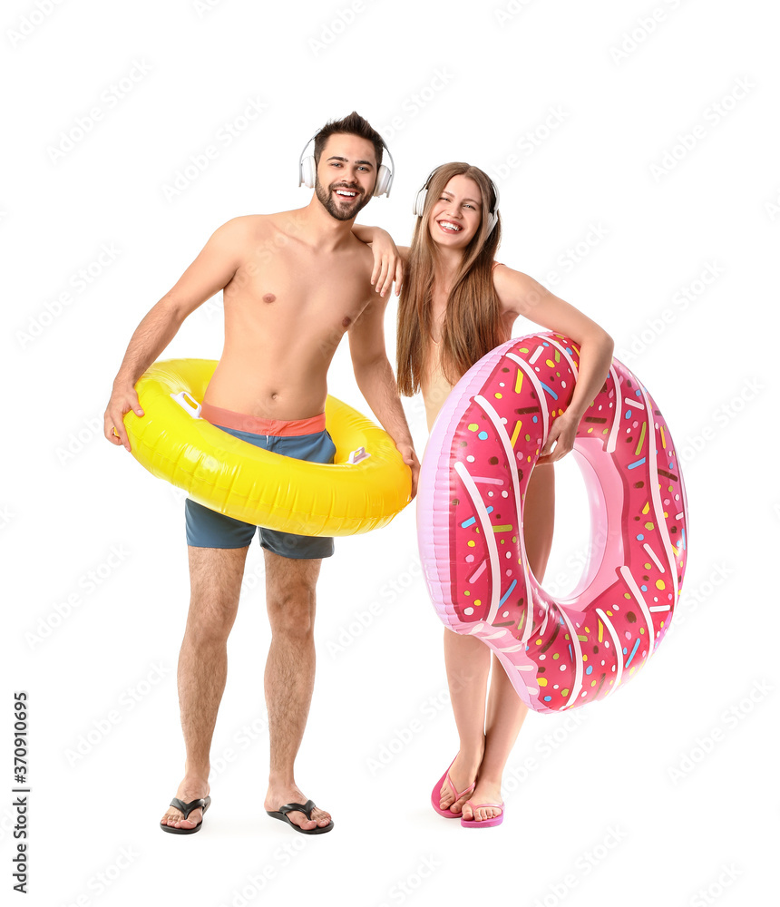 Young couple with headphones and inflatable rings on white background