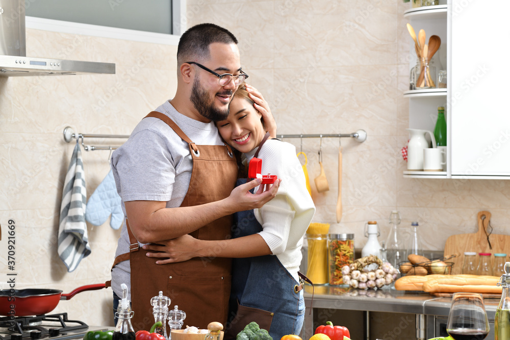 Asian man holding red box with ring making propose to his girlfriend in the kitchen