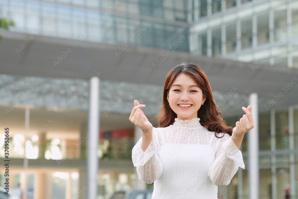 美丽的亚洲女人在城市背景上展示迷你心形手势。喜欢，爱和情人节