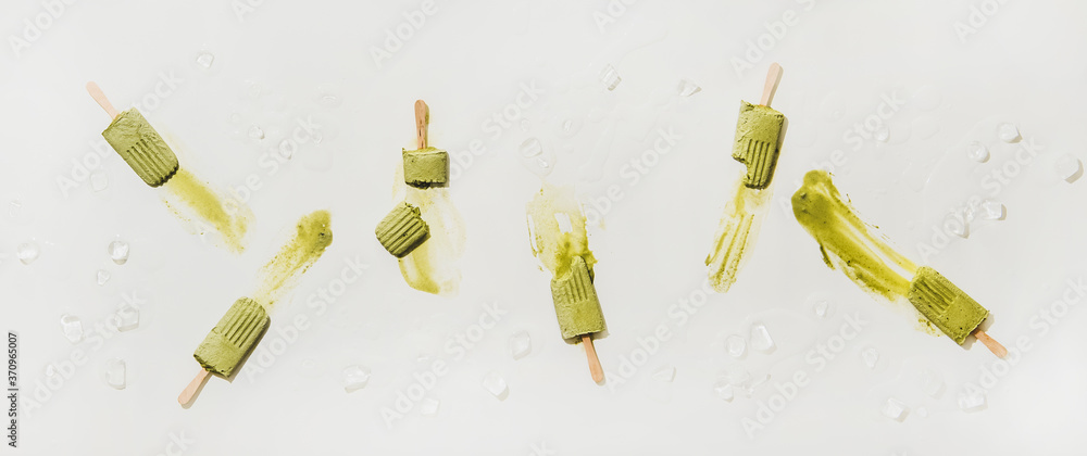 Green matcha coconut vegan ice cream popsicles. Flat-lay of melting matcha popsicles over plain whit