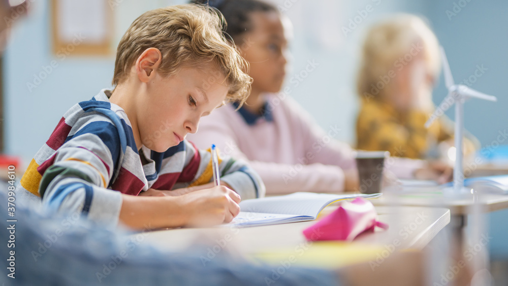 In Elementary School Classroom Brilliant Caucasian Boy Writes in Exercise Notebook, Taking Test and 