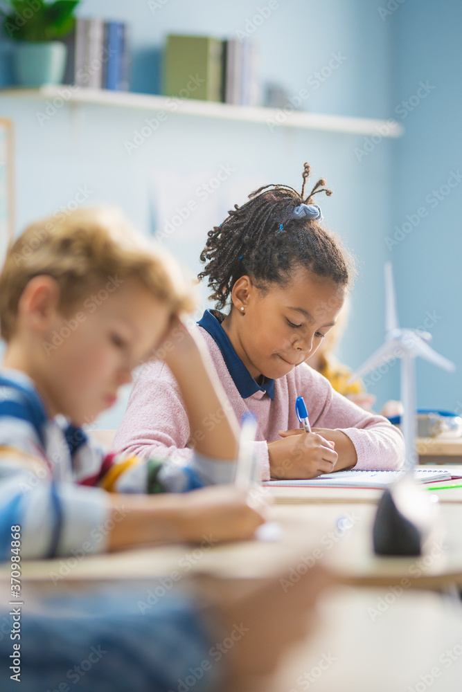 In Elementary School Classroom Brilliant Black Girl Writes in Exercise Notebook, Taking Test and Wri