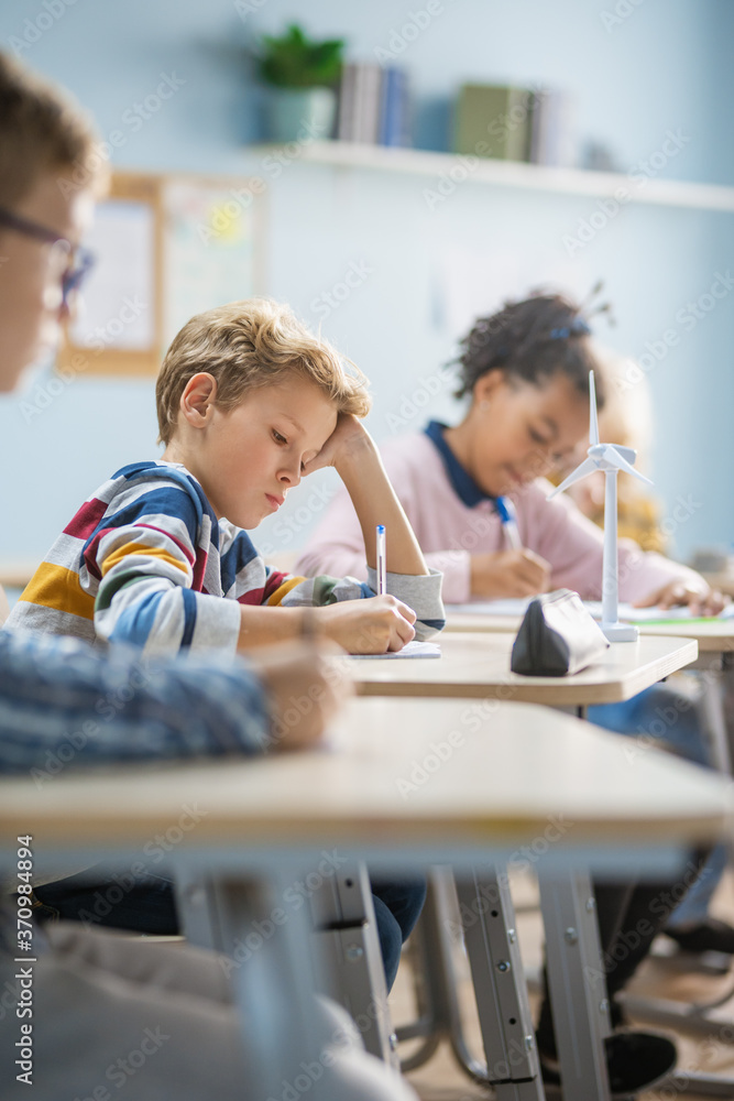 In Elementary School Classroom Brilliant Caucasian Boy Writes in Exercise Notebook, Taking Test and 