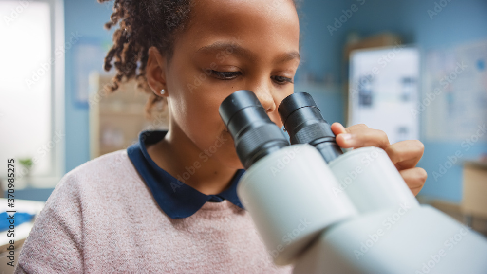 Portrait of Smart Little Schoolgirl Looking Under the Microscope. In Elementary School Classroom Cut