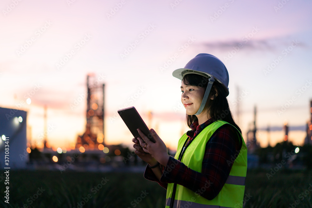 Asian woman petrochemical engineer working at night with digital tablet Inside oil and gas refinery 