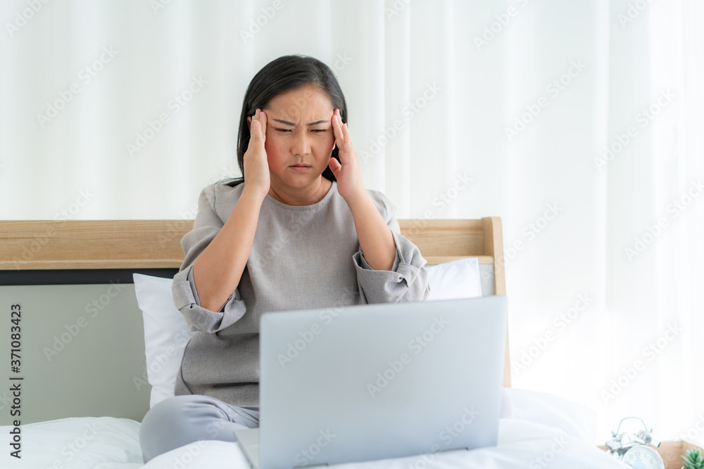 Asian woman in white bed speaking with doctor using tele health technology while sitting on a sofa a