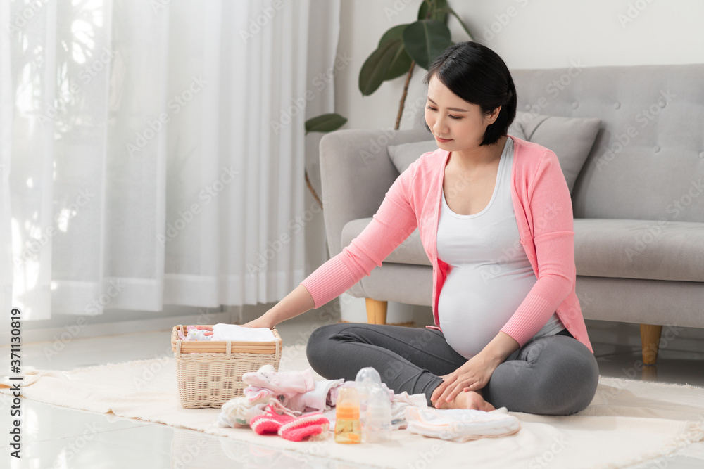 Beautiful pregnant asian woman packing and preparing baby clothes in basket for expectant new born b