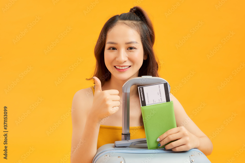 Portrait of young Asian woman with her passprt and luggage over orange background.