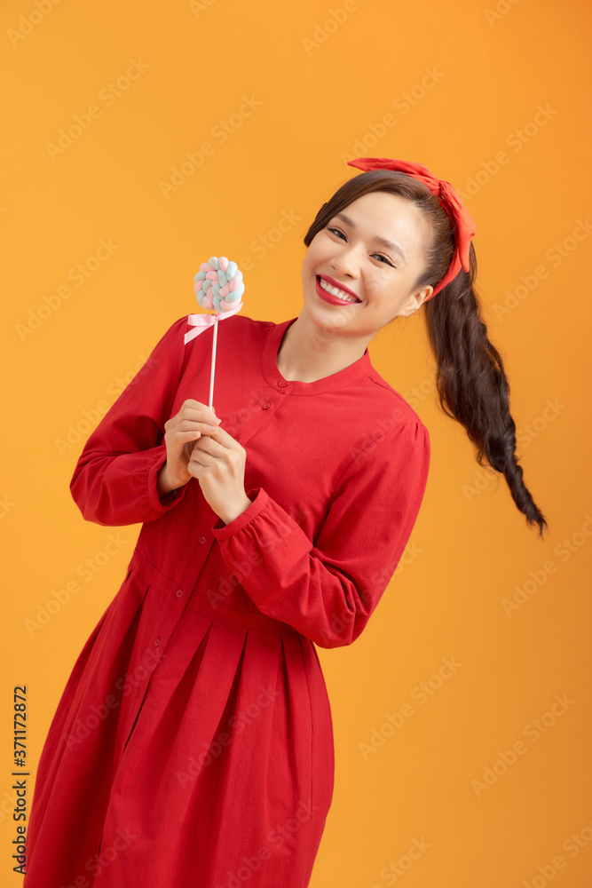 Laughing young woman holding lollipop over orange background and looking at camera