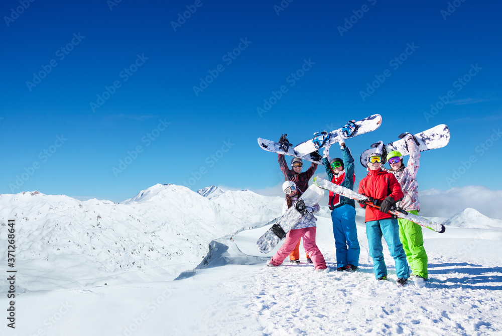 一大群年轻的单板滑雪运动员站在高山之巅将单板滑雪板举过头顶