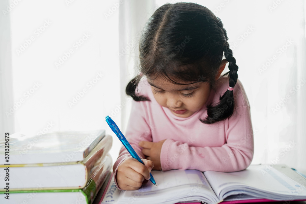 Asian student child girl writing on the paper book. Asian genius students doing homework at home. ed