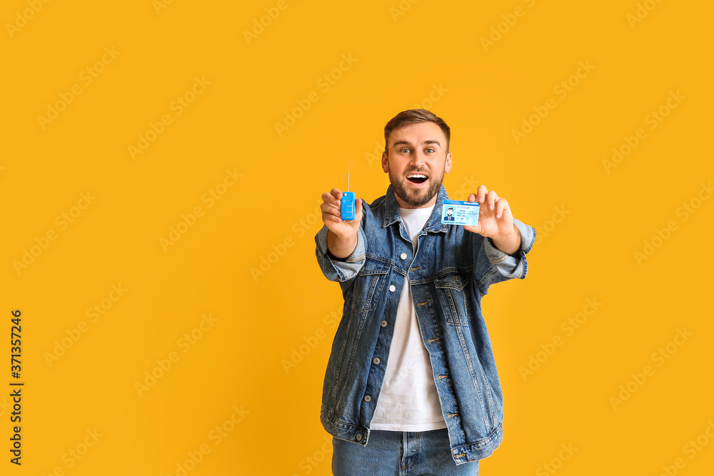 Happy young man with car key and driving license on color background