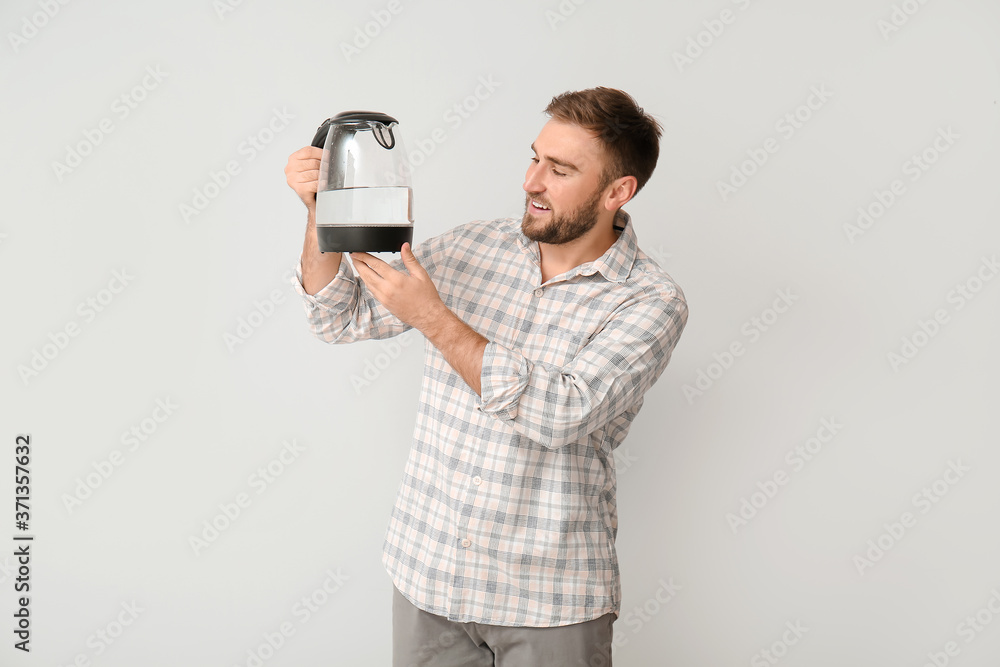 Young man with electric kettle on light background