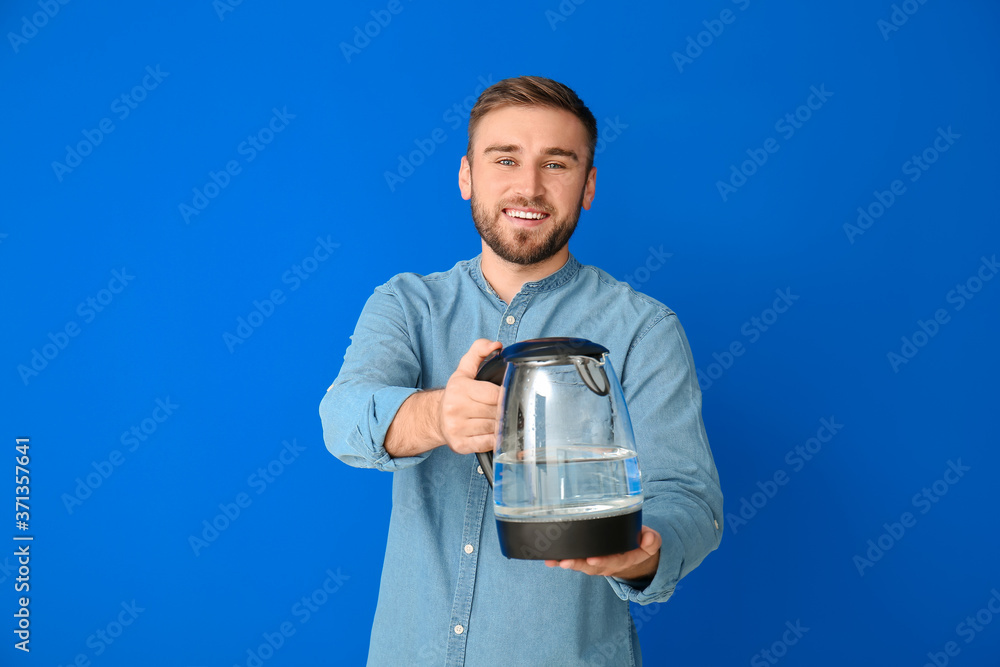 Young man with electric kettle on color background