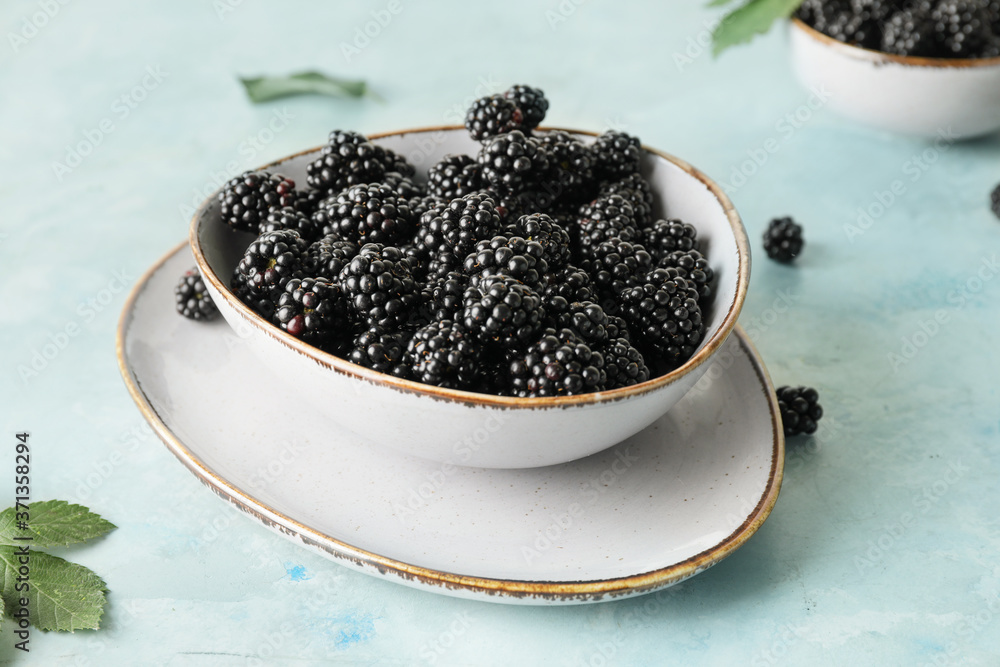 Bowl with tasty blackberry on color background