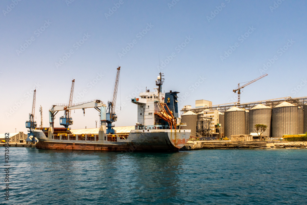 Large container ship being loaded with cargo in port in Port Sudan. Huge port cranes and row od grai