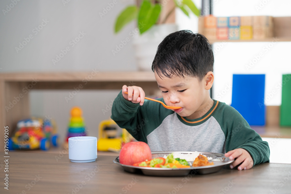 亚洲学生在教室里用他的幼儿园准备的食物托盘吃午饭