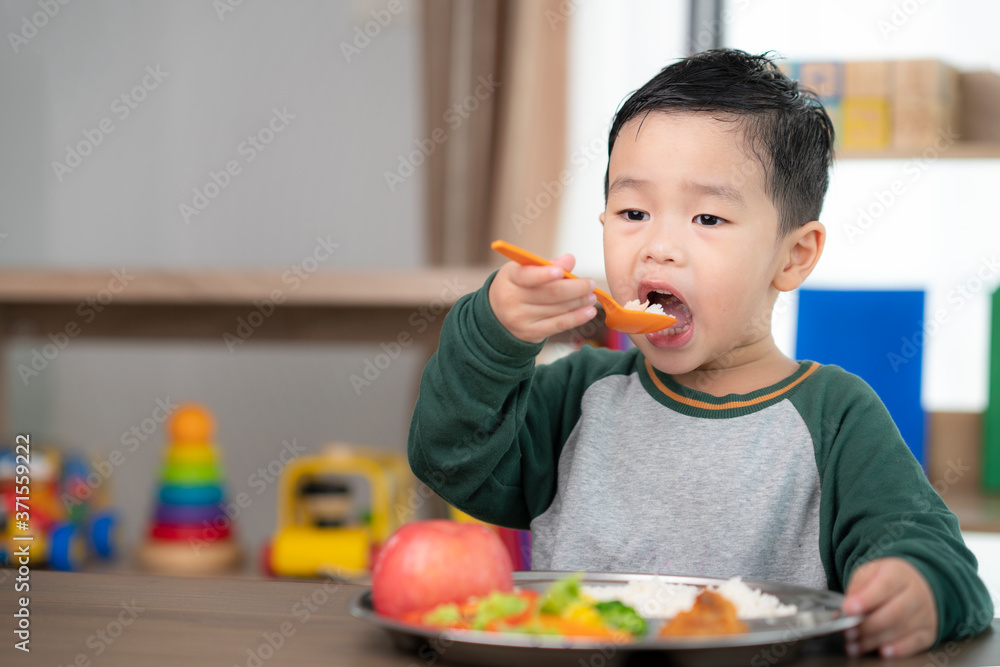 亚洲学生在教室里用他的幼儿园准备的食物托盘吃午饭