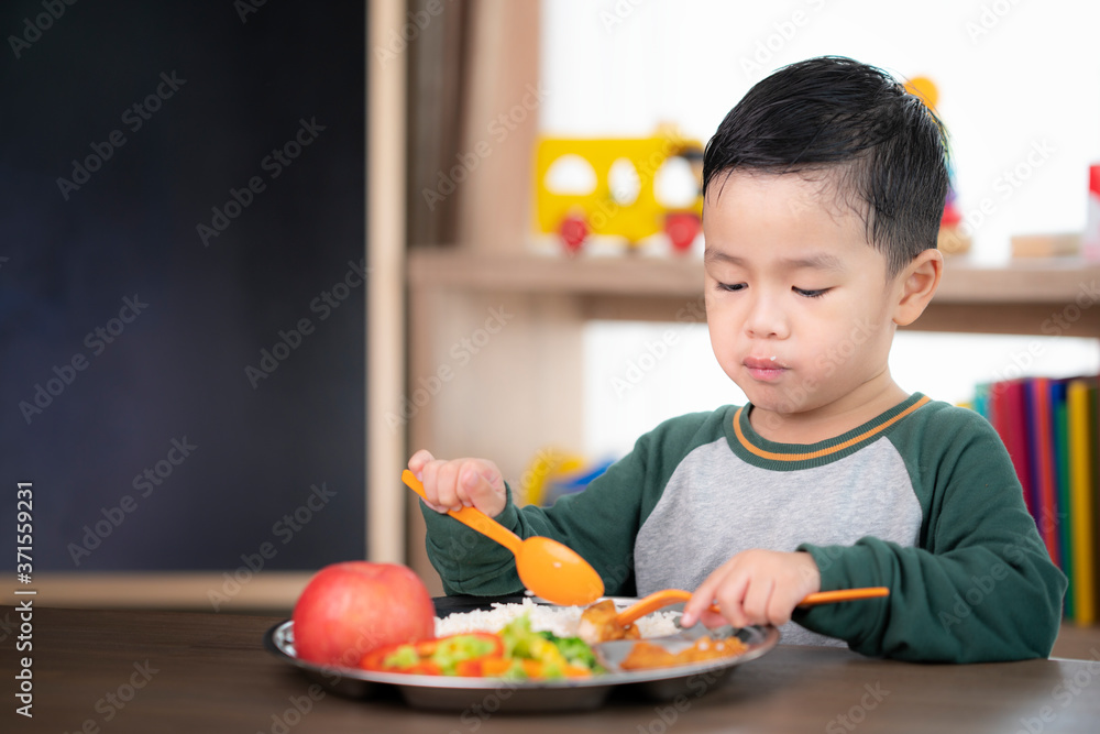 亚洲学生在教室里用他的学龄前儿童准备的食物托盘吃午饭