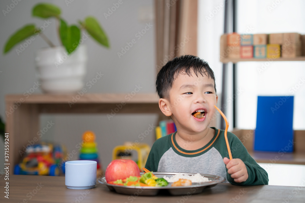 亚洲学生在教室里用他的学龄前儿童准备的食物托盘吃午饭