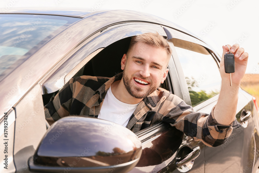 Happy young man with key sitting in his new car