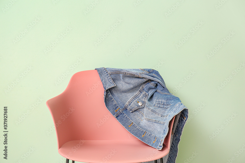 Jeans jacket on armchair against color background