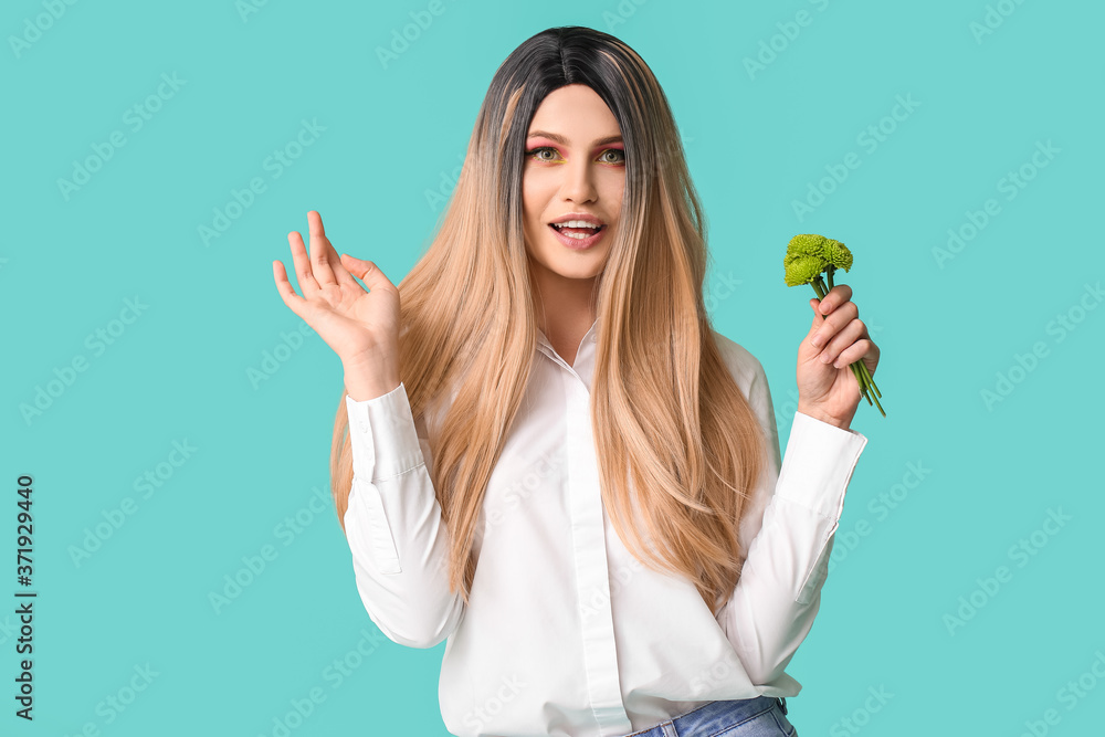 Beautiful young woman in wig and with flowers on color background