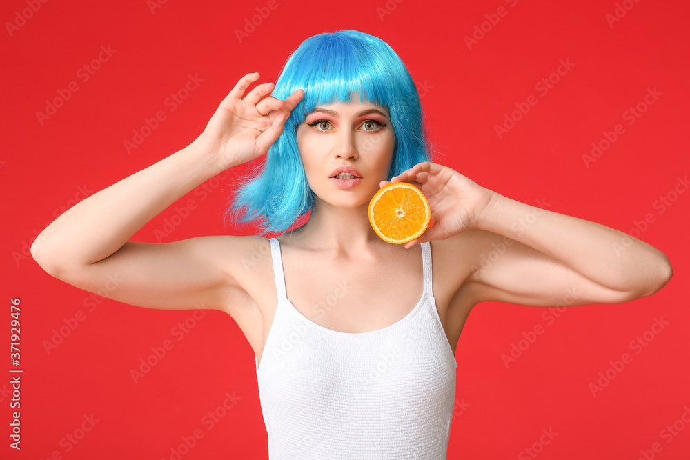 Beautiful young woman in wig and with orange on color background