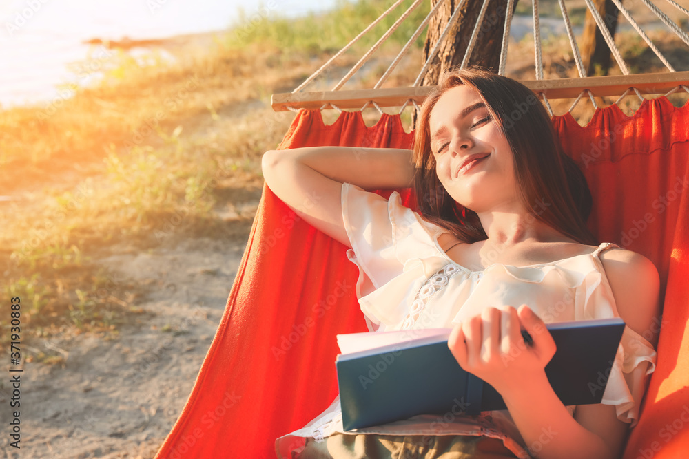 Young woman reading book while relaxing in hammock outdoors