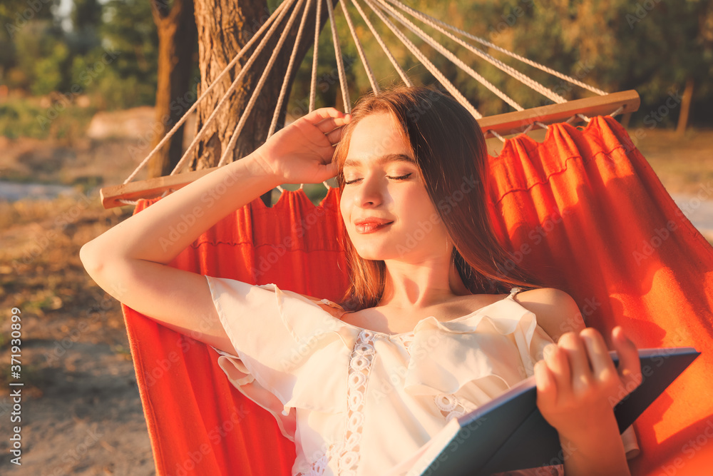 Young woman reading book while relaxing in hammock outdoors