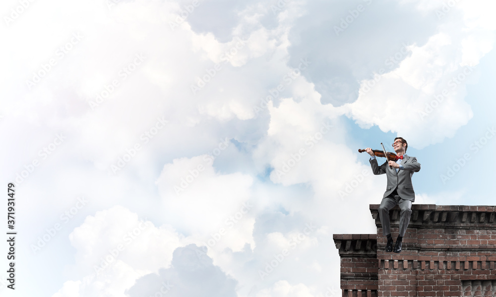 Handsome violinist in glasses on building edge play his melody