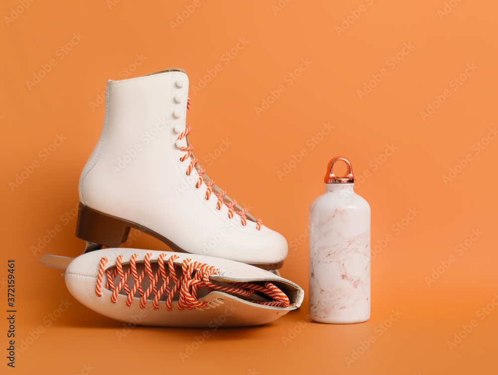 Ice skates with bottle for water on color background