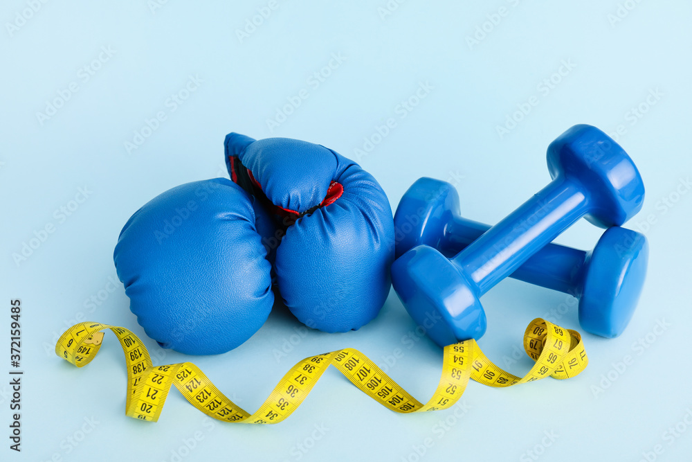 Boxing gloves with dumbbells and measuring tape on color background