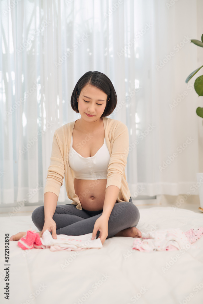 怀孕的亚洲妇女穿着小衣服看着她的孩子。