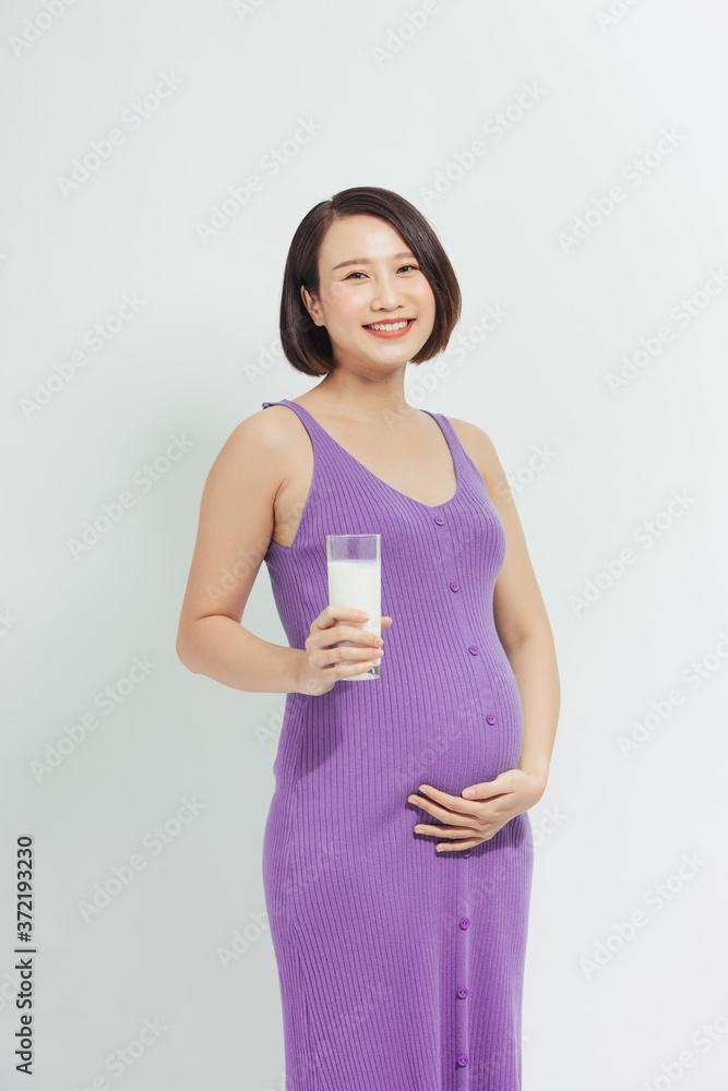 Happy pregnant woman drinking a glass of fresh milk and touching her belly with care