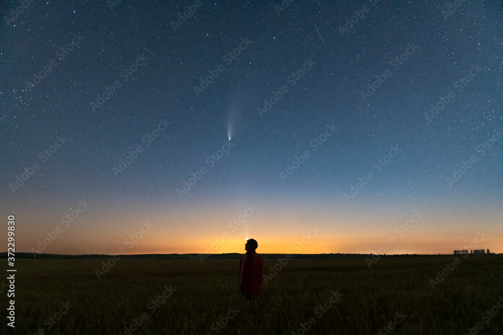 一名男子夜间站在城外田野上的剪影。尼奥维彗星的星空