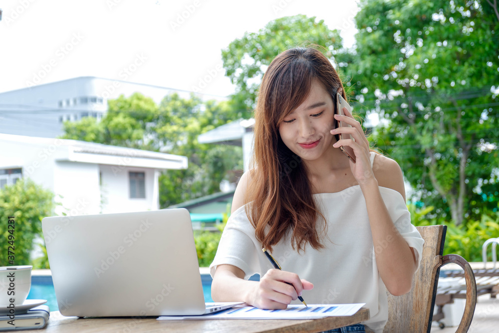 Portrait A young Asian woman doing business in the swimming pool on vacation, she is talking on the 